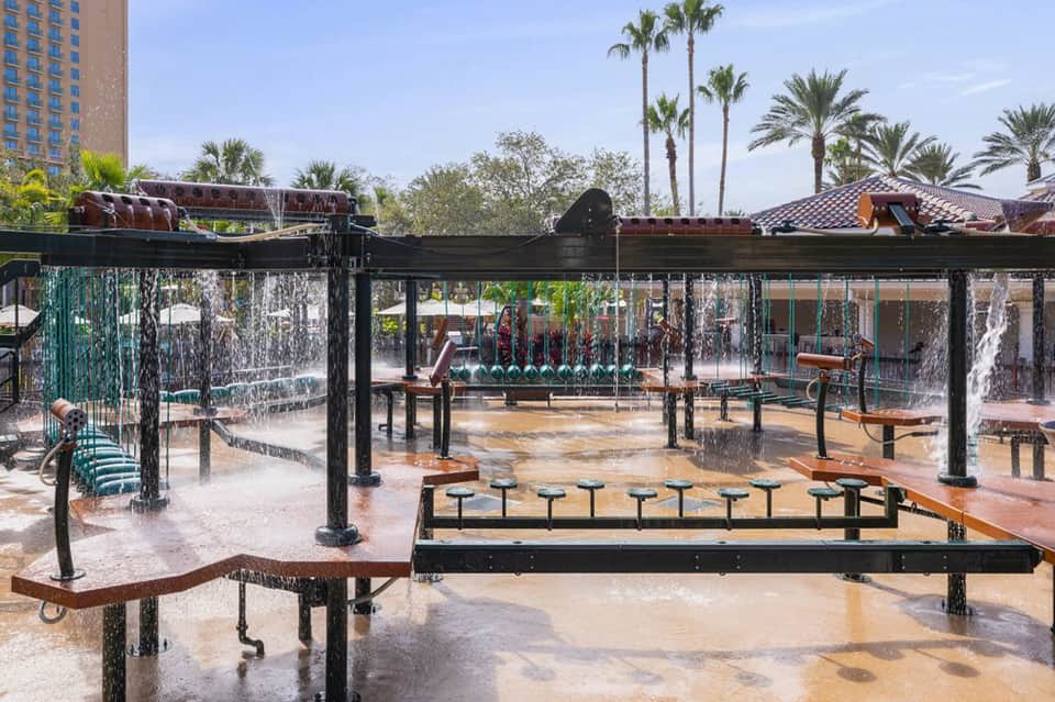 Interactive splash pad with water features, benches, and palm trees in resort courtyard setting