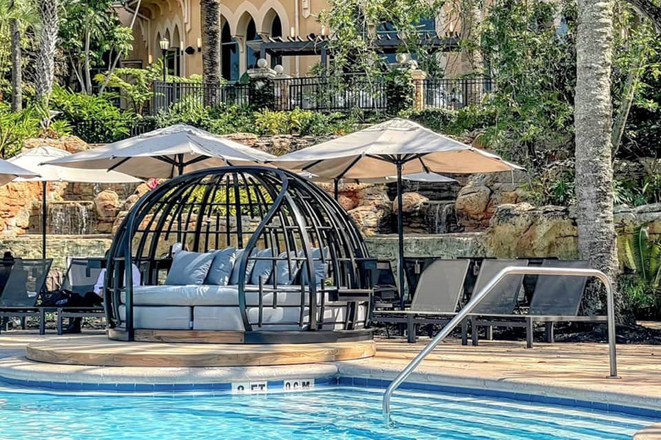 Resort pool area with distinctive black cage daybed, lounge chairs, and shade umbrellas