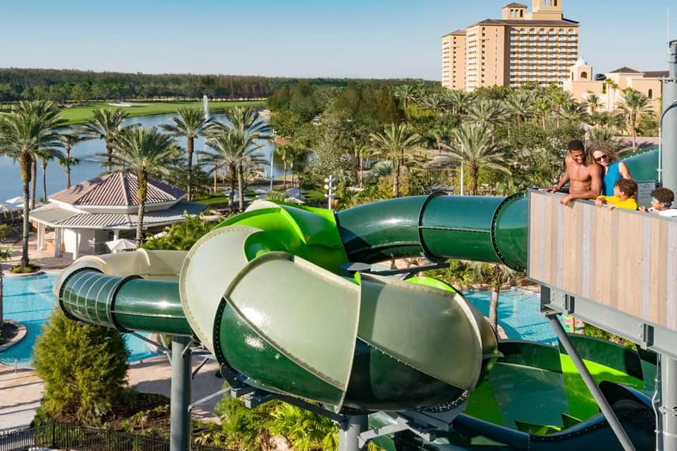 Green water slides at resort pool complex with palm trees and hotels in distance