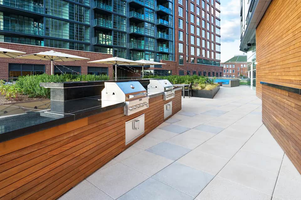 Rooftop terrace with built-in grills, umbrellas, planters, and urban skyline backdrop