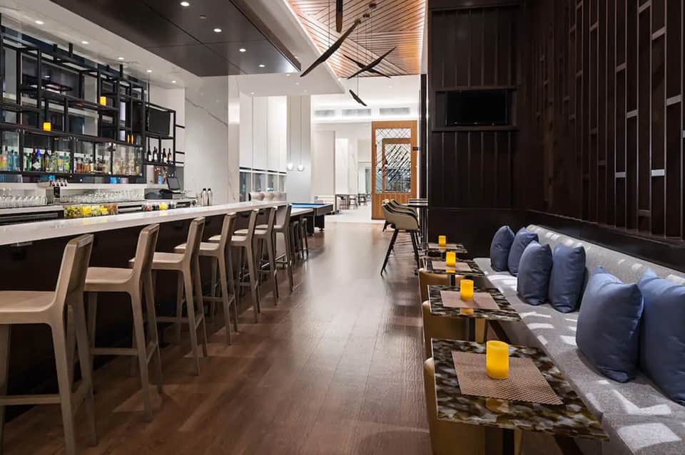 Contemporary lounge bar with bar seating, blue pillows, and modern wood ceiling detail