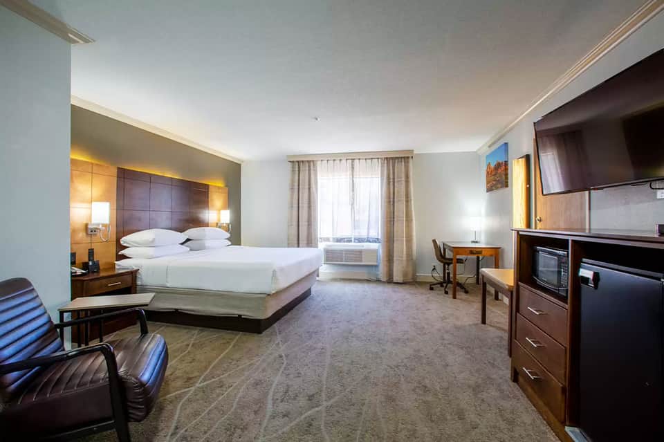 Spacious hotel suite with king bed, dark wood headboard, and contemporary furnishings