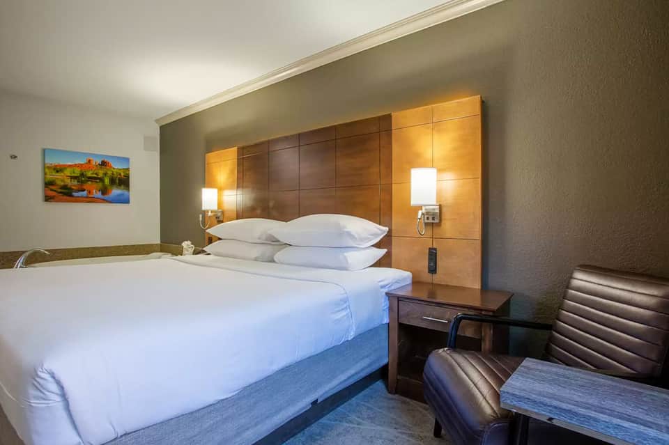 Hotel bedroom with white bedding, wood headboard, and side chair
