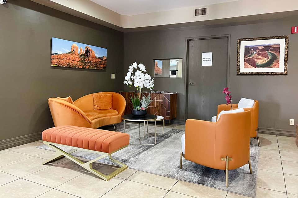 Contemporary hotel lobby with gray walls, orange leather chairs, white flowers, and southwestern landscape artwork