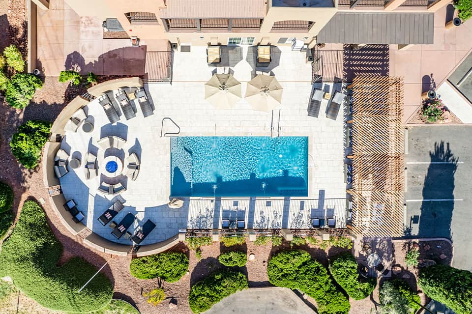 Aerial view of resort pool deck with blue swimming pool, lounge chairs, and manicured grounds