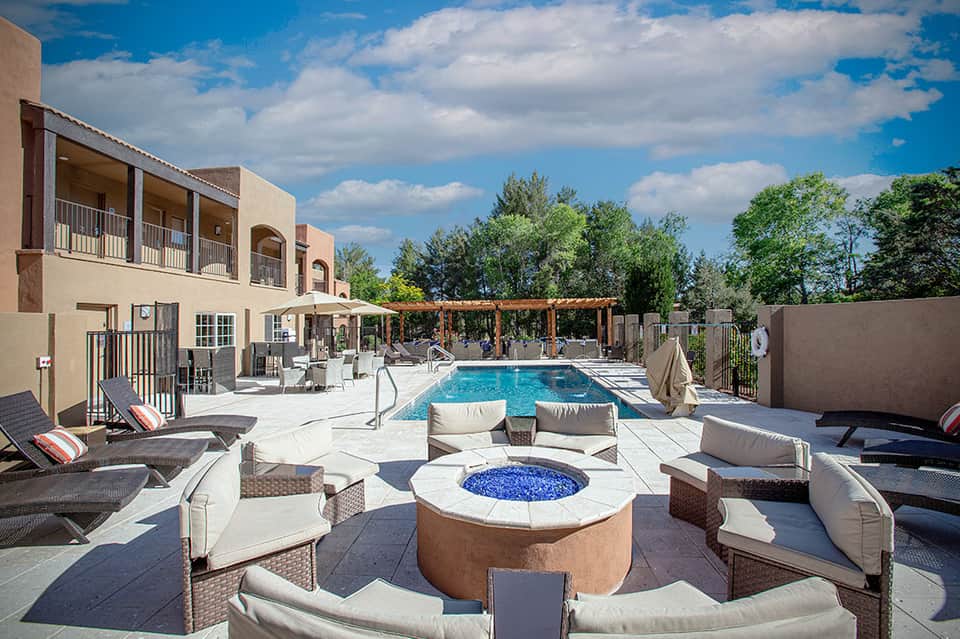 Resort pool deck with fire pit, lounge chairs, pergola, and modern architecture under blue sky
