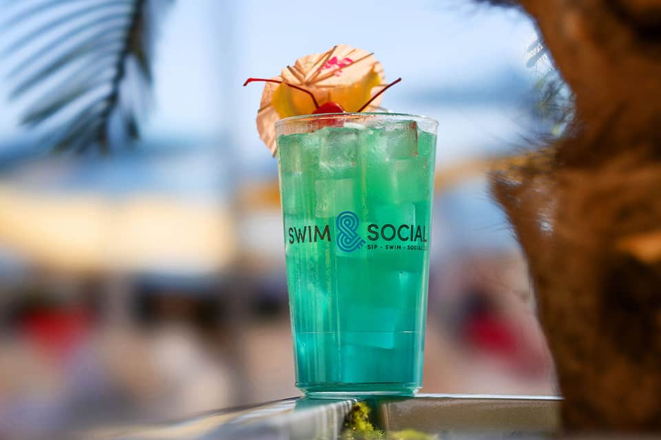 Tropical cocktail with green liquid and decorative fruit garnish at beachfront bar