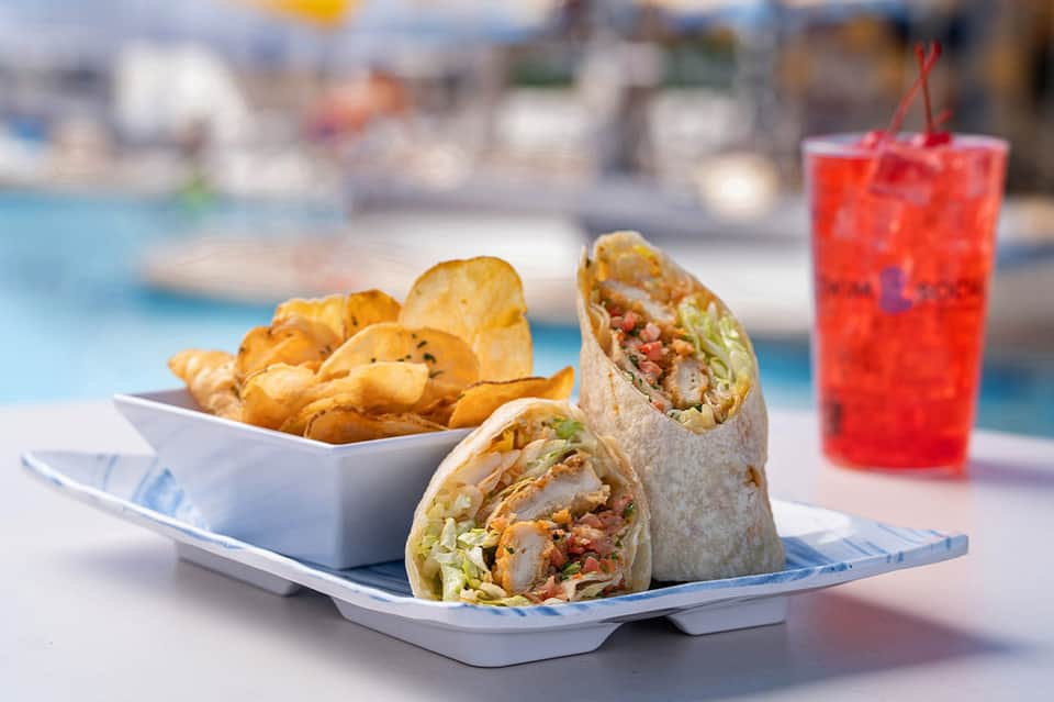 Poolside food plate with wraps and fried plantains, tropical drink, blurred resort background