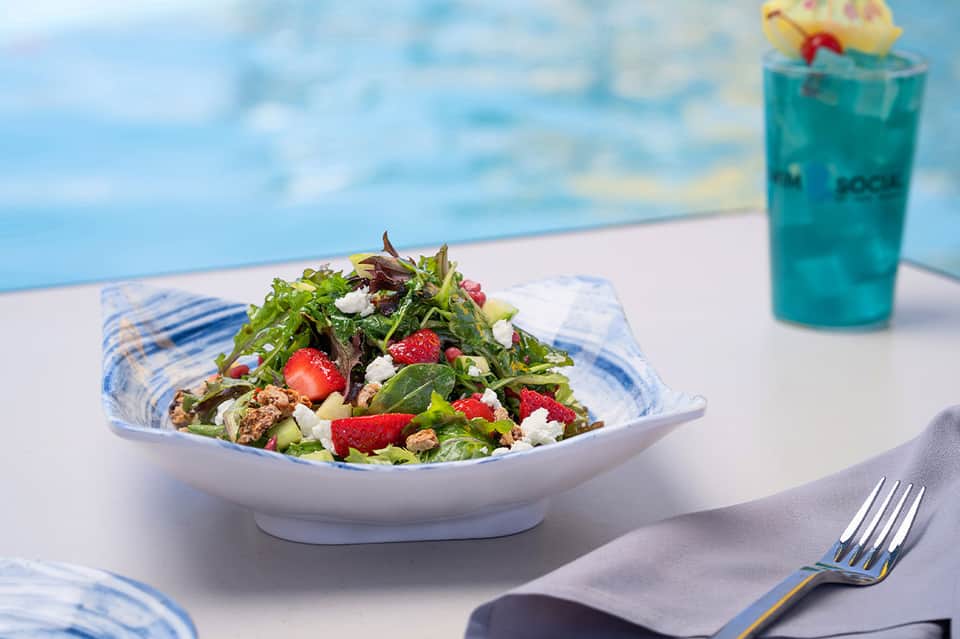 Fresh salad with berries and greens served poolside with turquoise beverage in background