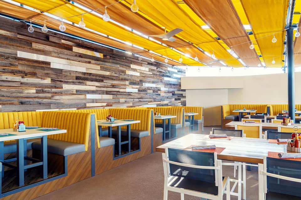 Modern rooftop restaurant with yellow fabric ceiling, wood accent wall, and bright seating areas