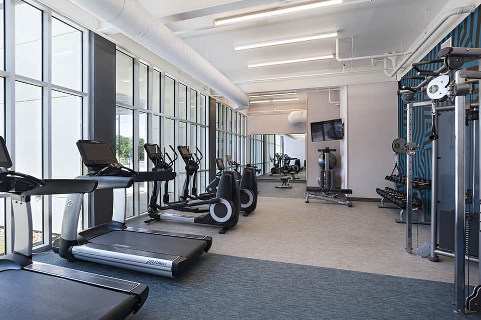 Modern fitness center with treadmills, stationary bikes, gym equipment, and floor-to-ceiling windows