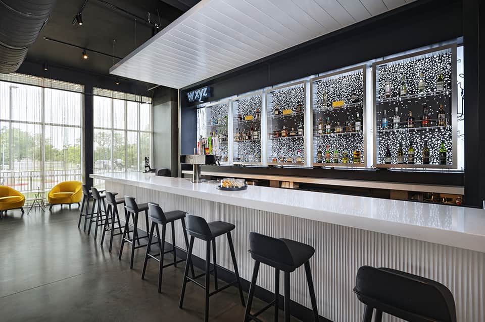 Modern hotel bar with black and white design, decorative wall panels, bar seating, and large windows