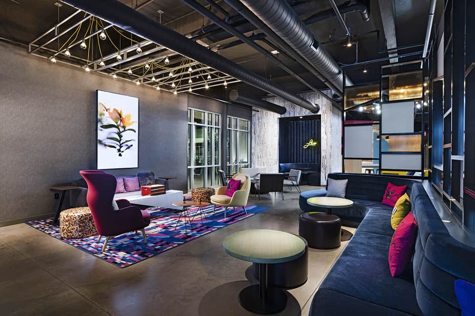 Modern hotel lounge with industrial ceiling, colorful furnishings, and vibrant accent pillows