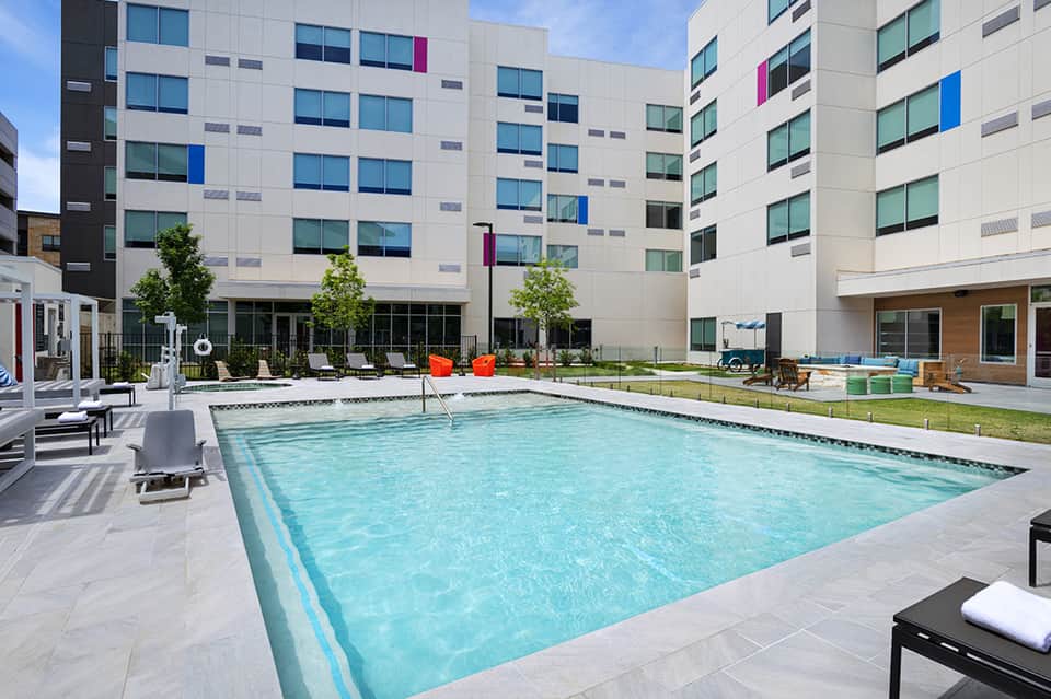 Modern resort pool surrounded by contemporary apartment buildings with loungers and deck space