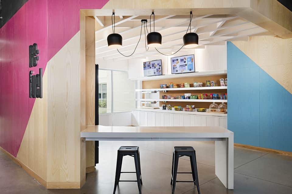 Modern resort café with pink and blue accents, wooden shelving, pendant lights, and counter seating