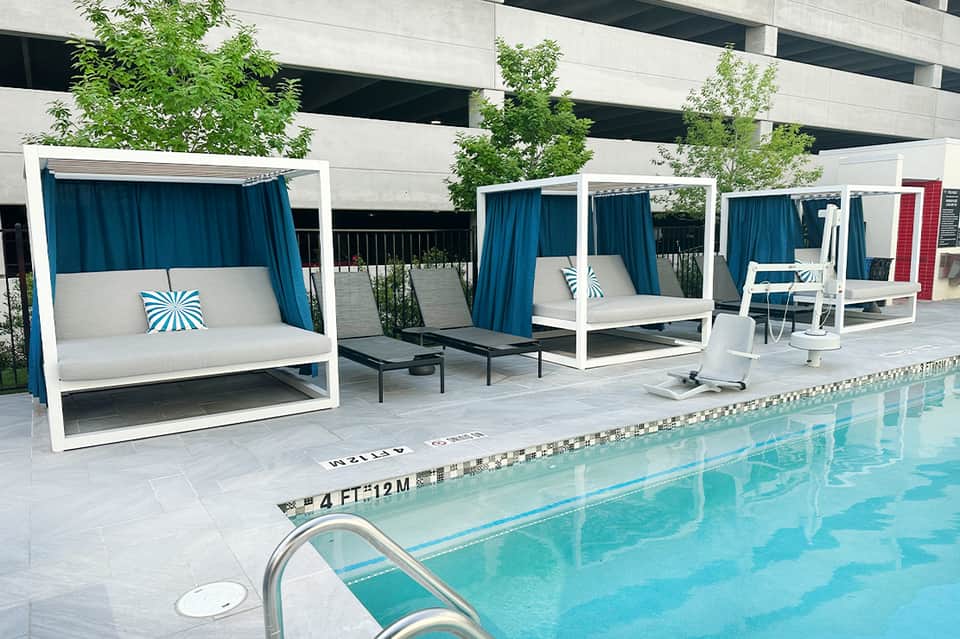 Contemporary pool deck with cabanas, white pergolas, blue curtains, and lap pool