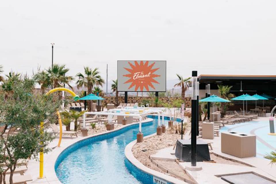 Lazy river pool winding through resort deck with turquoise umbrellas, palm trees, and modern structures