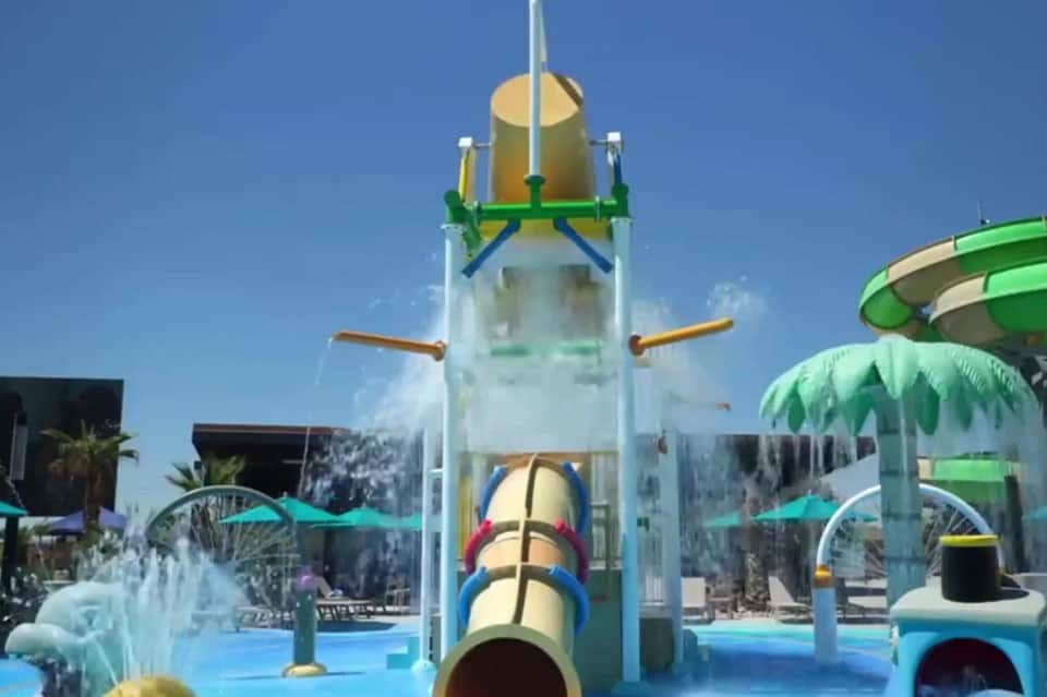 Colorful water park with tall blue splash tower, water slides, umbrellas, and clear blue sky