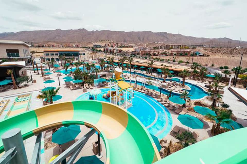 Aerial view of expansive resort water park with multiple pools, slides, and palm trees in desert landscape