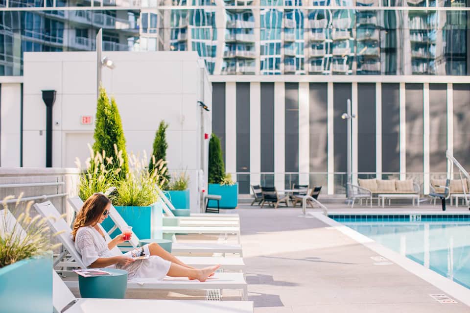Woman relaxing on lounge chair by rooftop pool with modern high-rise buildings in background