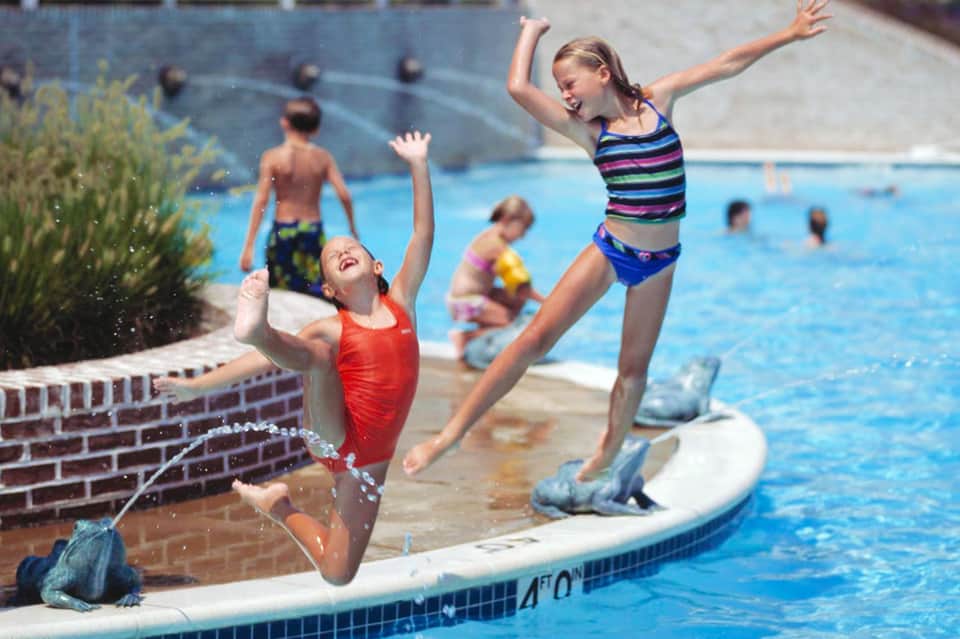 Children jumping into a swimming pool at a resort during summer recreation activities