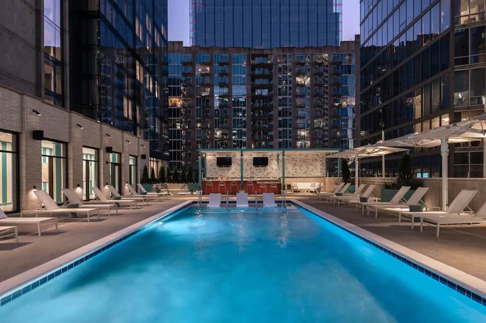 Urban hotel pool at night surrounded by lounge chairs and modern high-rise buildings
