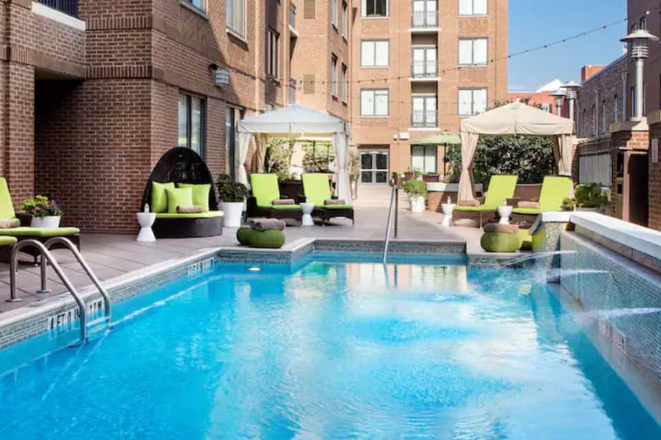 Urban rooftop pool with lime green loungers, umbrellas, and brick apartment buildings surrounding