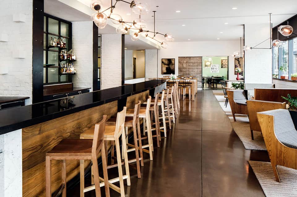 Contemporary restaurant and bar interior with white brick, wooden seating, pendant lighting, and open layout