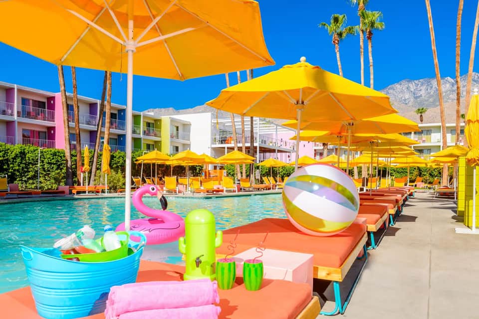 Colorful poolside with yellow umbrellas, pink flamingo float, and vibrant resort buildings