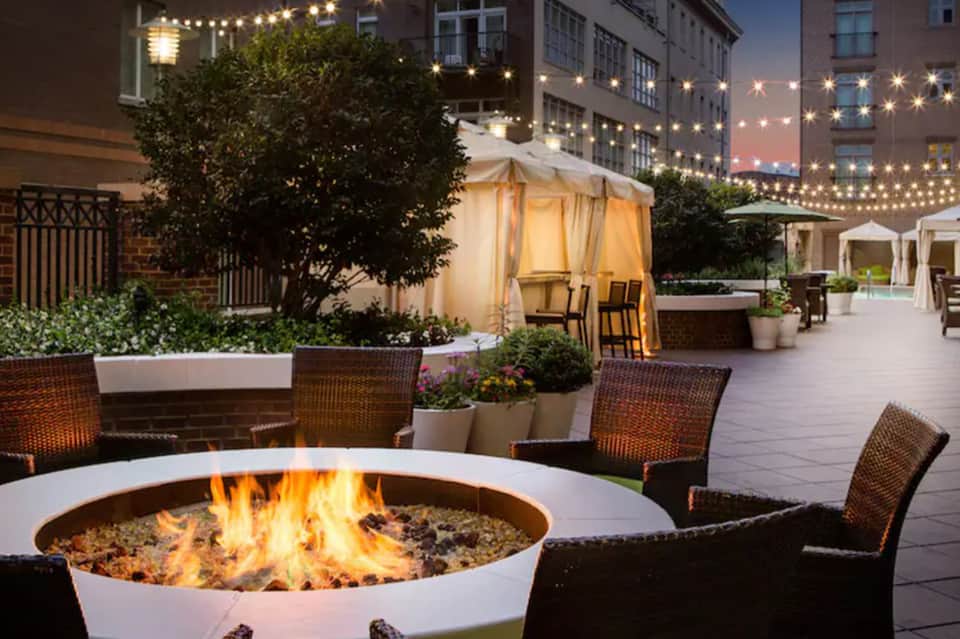 Rooftop fire pit lounge at night with string lights, tent, and cocktail seating
