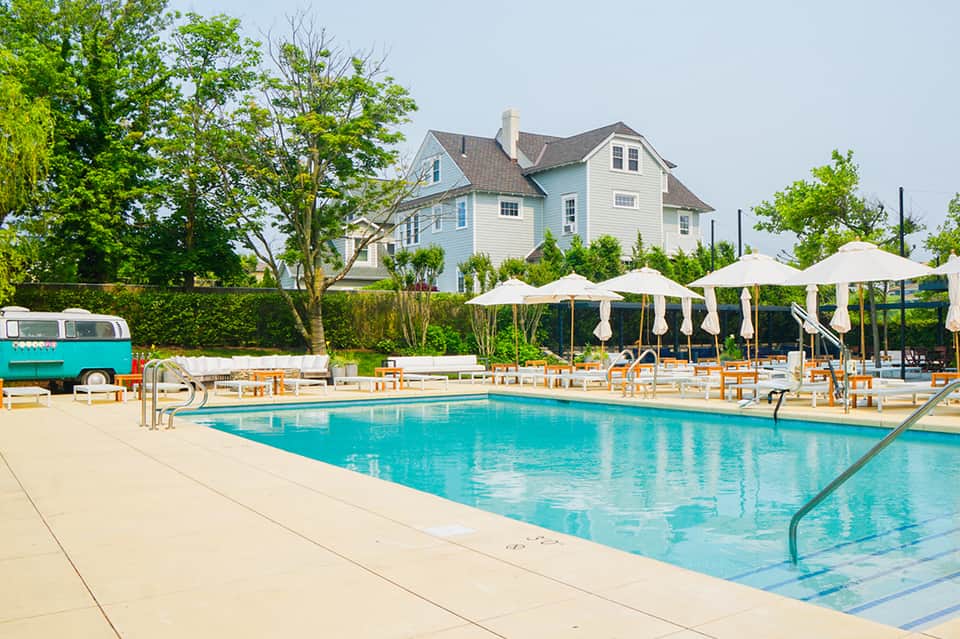 Rectangular lap pool with cream umbrellas, wooden lounge chairs, and farmhouse-style building