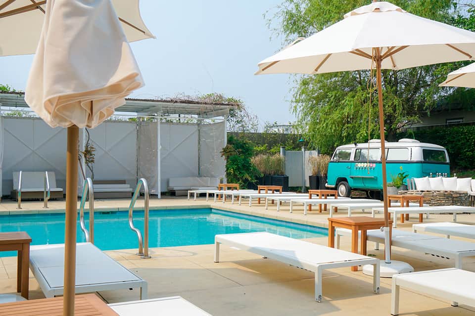 Resort pool area with turquoise water, white lounge chairs, umbrellas, and vintage camper van