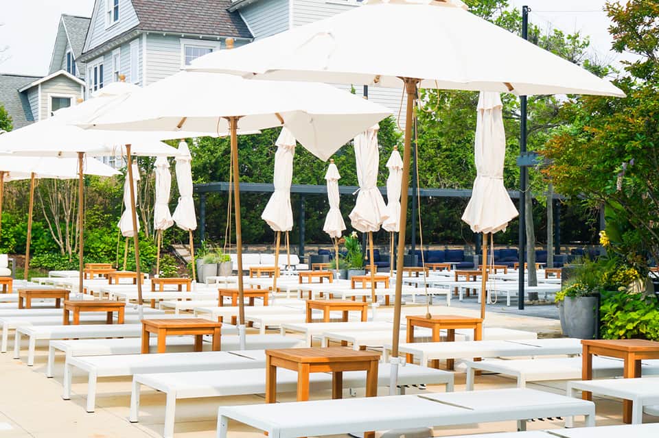 Outdoor patio with white loungers under cream umbrellas and trees