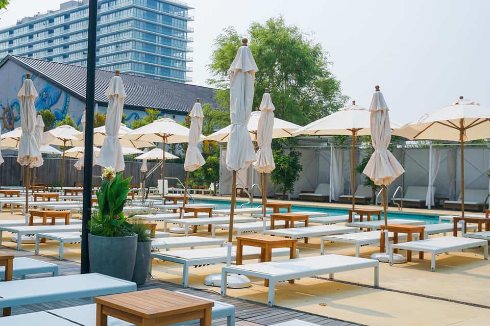 Upscale poolside lounge area with wooden daybeds, white umbrellas, and modern building