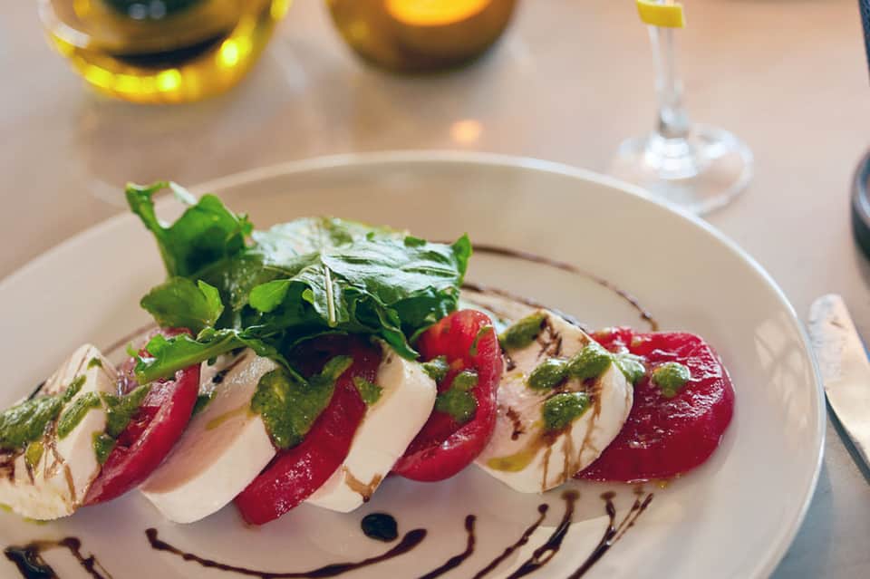 Gourmet plated dish with beets, mozzarella, and microgreens with wine glasses nearby