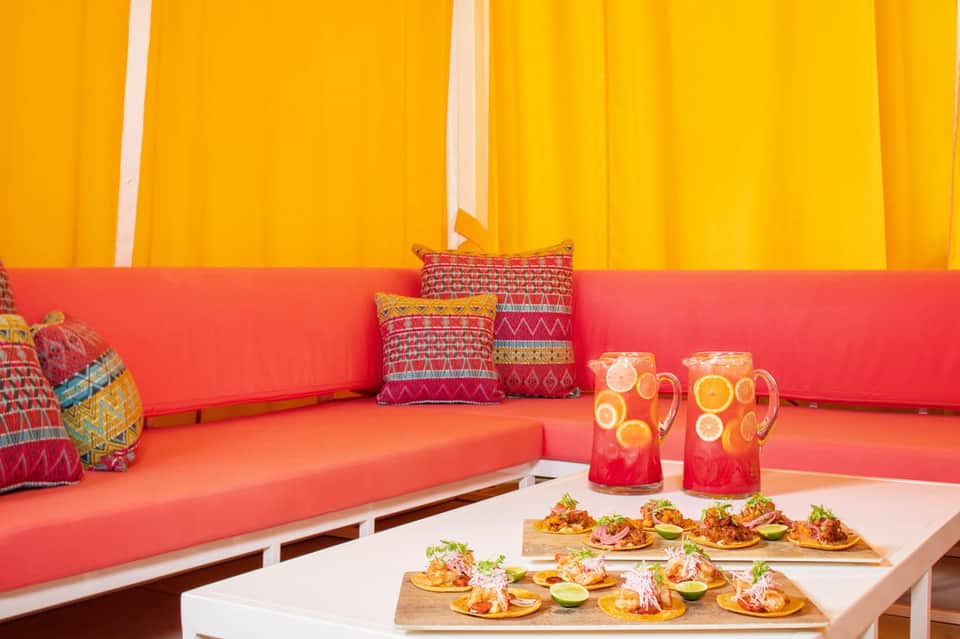 Colorful lounge area with bright yellow and coral cushioned seating, patterned pillows, and refreshment pitchers