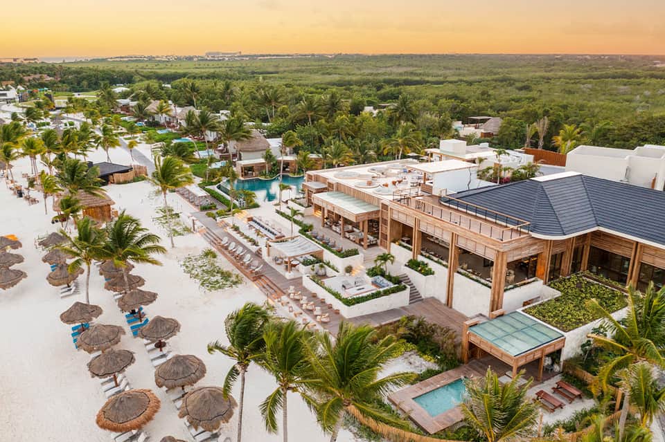 Aerial view of beachfront resort with white sand, palm trees, and wooden structures