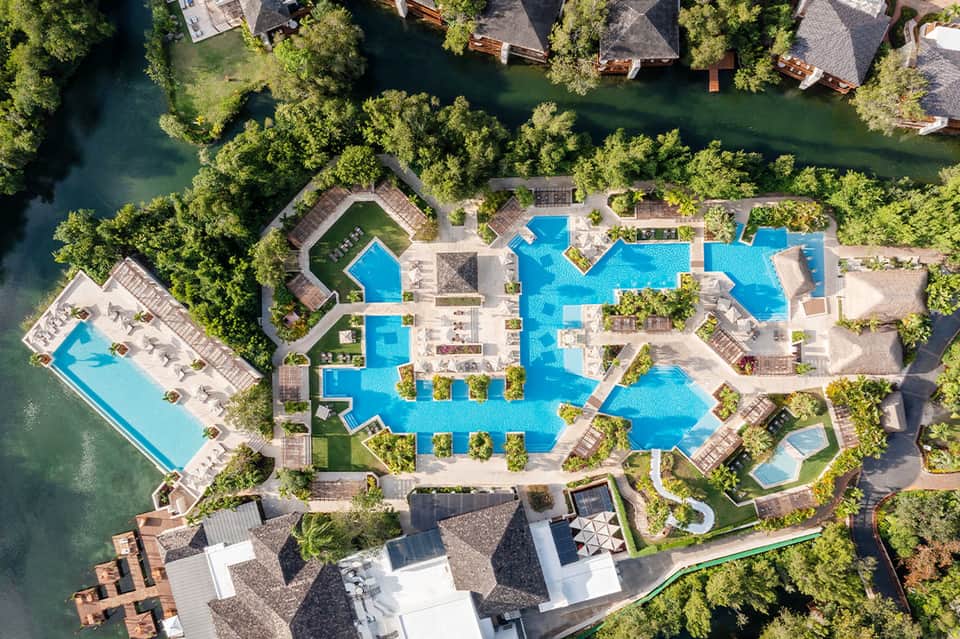 Aerial view of resort with multiple swimming pools, surrounding lush greenery and waterfront buildings