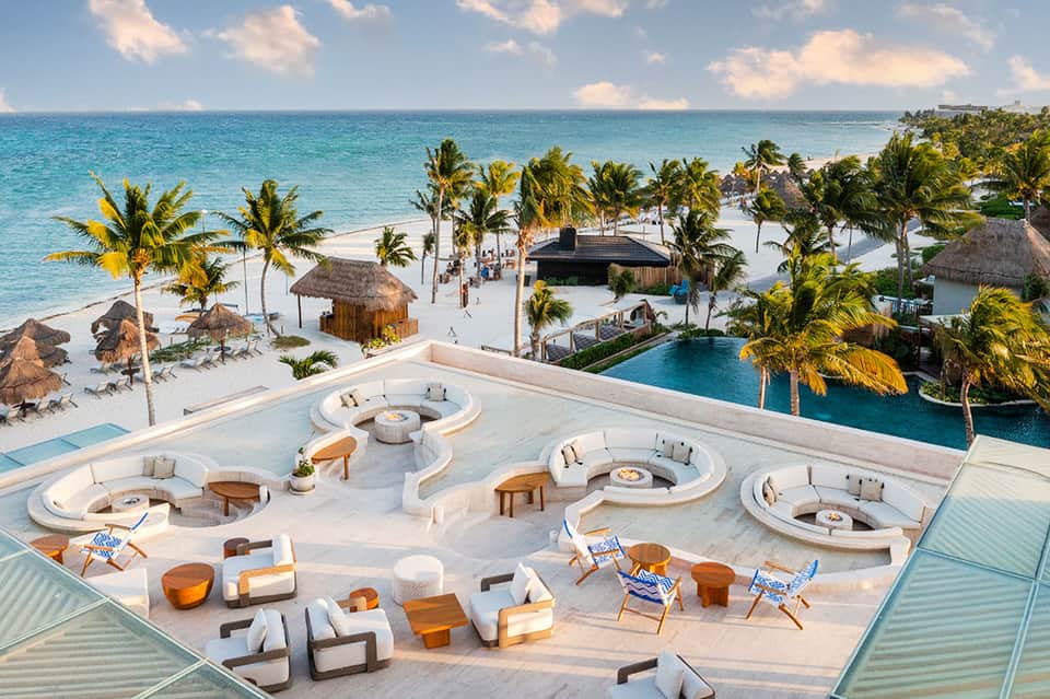 Aerial view of luxury beachfront resort with circular fire pits, pools, and palm trees