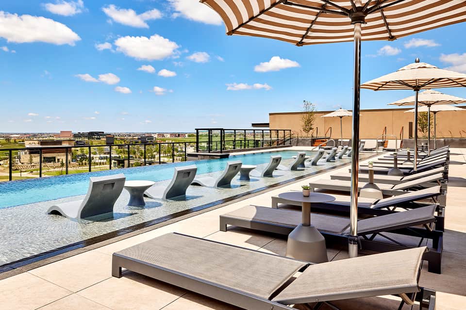 Modern rooftop pool with striped umbrellas, loungers, and panoramic landscape views