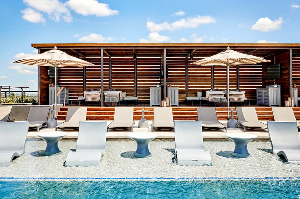 Beach cabanas with umbrellas, lounge chairs, wooden structure, and ocean view
