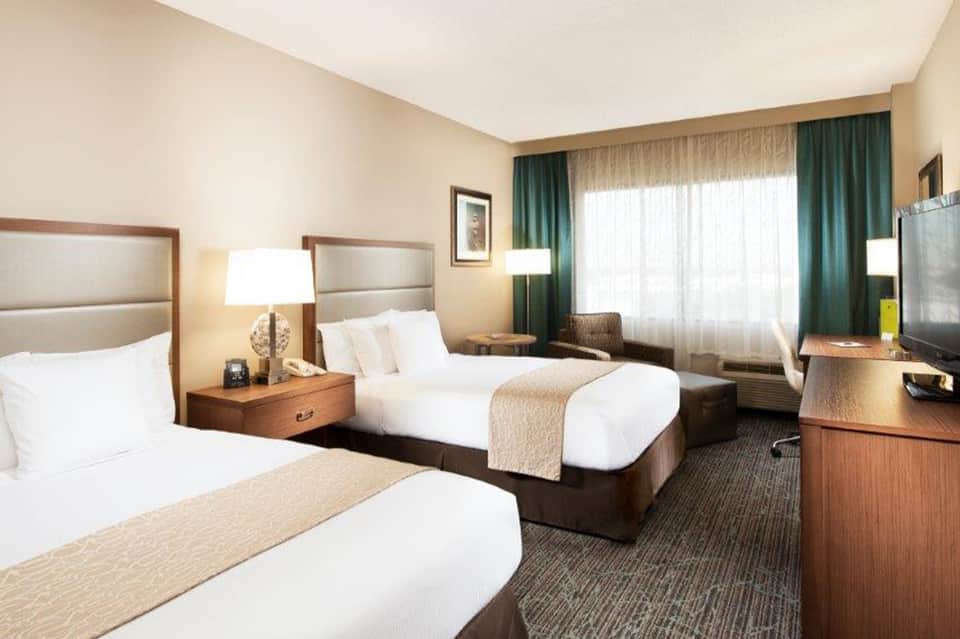 Hotel guest room with two queen beds, green curtains, wood furnishings, and modern decor