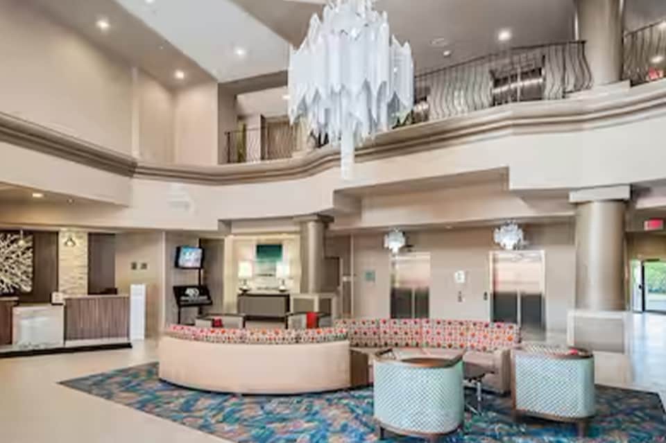 Modern hotel lobby with two-story atrium, chandelier, pink accent wall, and service desk