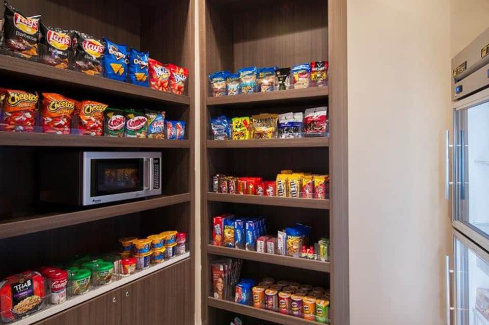In-room snack pantry shelves stocked with chips, candy, beverages, and microwave