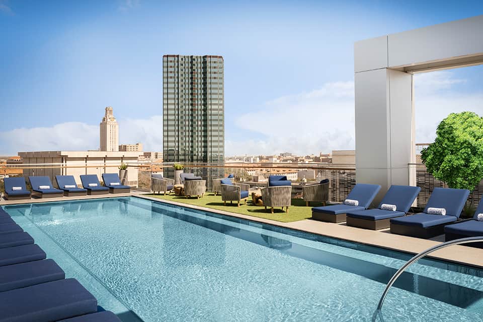 Rooftop infinity pool with city skyline views, blue loungers, and modern urban architecture