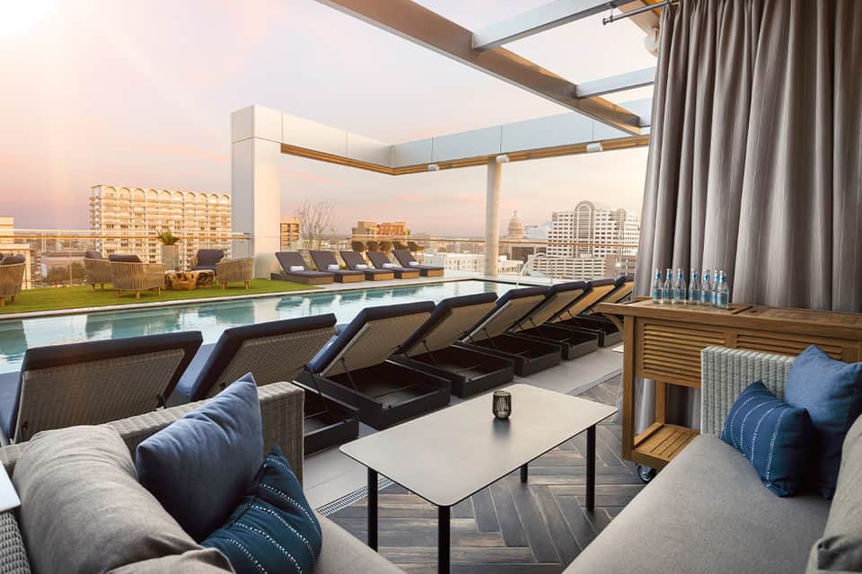 Rooftop pool with loungers, city skyline views, retractable shade, and lounge seating
