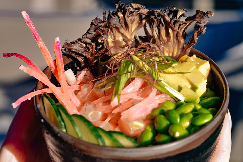 Artfully plated dish with seaweed, pink radish, and green vegetables in ceramic bowl