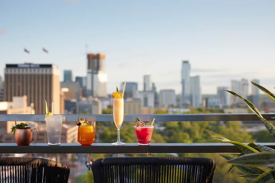 Rooftop bar with cocktails and city skyline view featuring multiple drink glasses