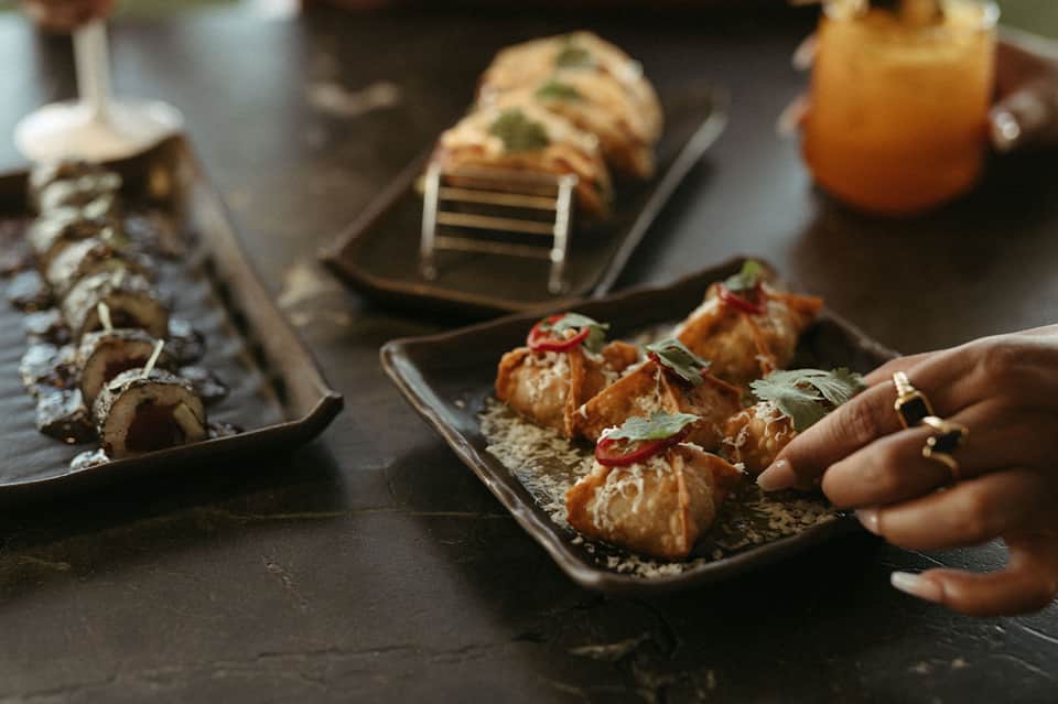 Fine dining appetizers on black slate plates including sushi rolls and garnished seafood bites