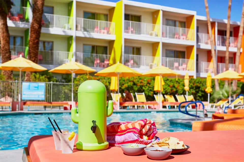 Colorful poolside setup with bright green beverage dispenser, snacks, and towels at vibrant resort with yellow umbrellas